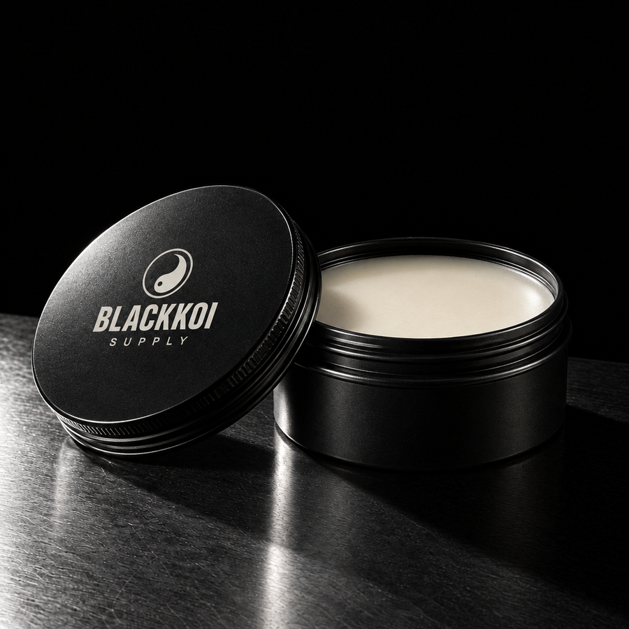 Aftercare balm tin in BlackKoi Supply packaging, lid off, on brushed steel